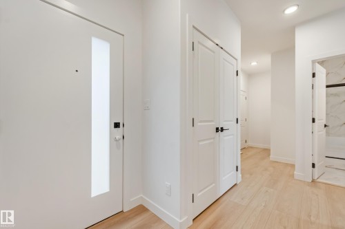 Entryway featuring a contemporary white door with frosted glass panel, light wood-finish flooring, recessed lighting, and crisp white walls - 4636 18 Avenue, Edmonton, AB 