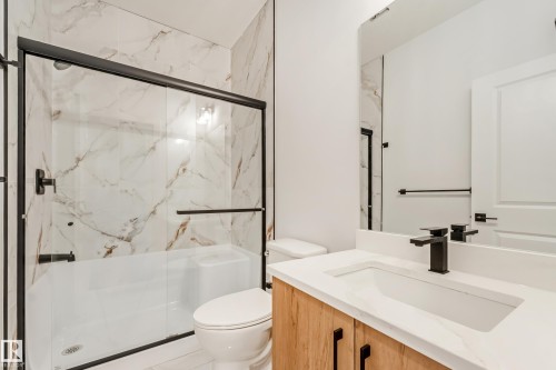 Bathroom featuring a bathtub with a clear glass sliding door, large format tile surround, and matte black fixtures - 4636 18 Avenue, Edmonton, AB 