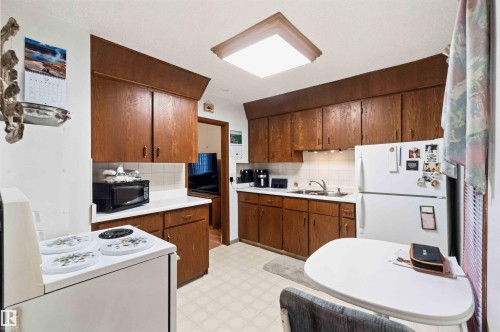 Kitchen featuring wood-finish cabinetry, white tile backsplash, and a white laminate countertop - 12016 61 Street, Edmonton, AB 