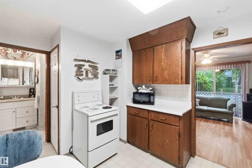 Kitchen featuring wood cabinetry, white countertops, white tile backsplash, and a white range - 12016 61 Street, Edmonton, AB 
