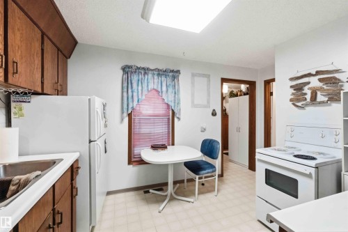 Kitchen featuring wood cabinetry, white countertops, a stainless steel sink, and white appliances - 12016 61 Street, Edmonton, AB 