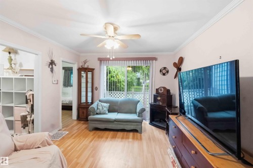 Light wood-finish flooring complements the interior space featuring a ceiling fan, crown molding, and white trim - 12016 61 Street, Edmonton, AB 