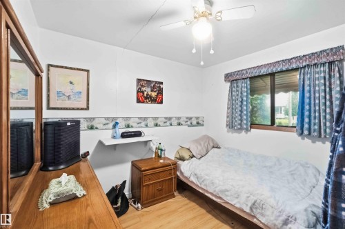 Room featuring wood-finish flooring, a ceiling fan with integrated lighting, a window with curtains, and white wall finishes - 12016 61 Street, Edmonton, AB 