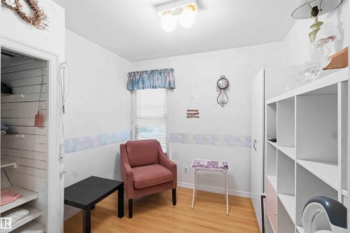 Wood-finish flooring throughout, featuring a window with blind, overhead flush-mount lighting, and an open closet with built-in shelving - 12016 61 Street, Edmonton, AB 