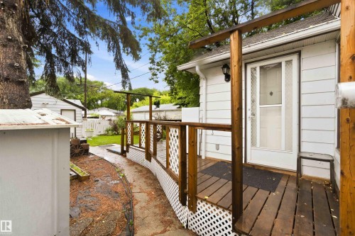 Exterior featuring white siding, a wood deck with railing, and a side entrance with a storm door - 12016 61 Street, Edmonton, AB 