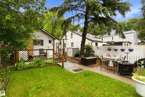 Expansive backyard featuring a green lawn, wood deck with lattice railing, mature trees, and a white picket fence - 12016 61 Street, Edmonton, AB 