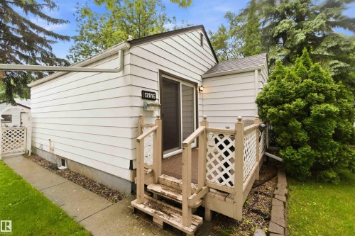 Exterior siding in a light finish, featuring a side entrance with a wooden deck and railing - 12016 61 Street, Edmonton, AB 