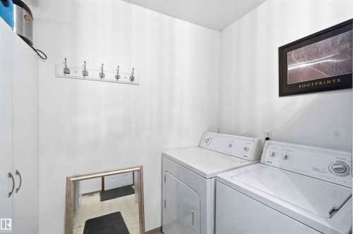 Laundry area featuring a side-by-side washer and dryer, white cabinetry, and a wall-mounted coat rack with five hooks - 12016 61 Street, Edmonton, AB 