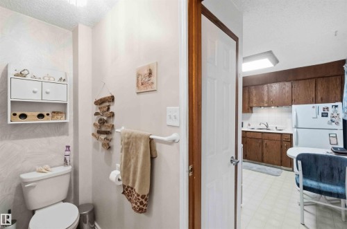 Compact bathroom featuring a white toilet and wall-mounted shelving - 12016 61 Street, Edmonton, AB 