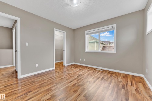 Spacious room featuring wood-finish flooring, neutral-toned walls, a large window with white blinds, and two doorways - 1328 80 Street, Edmonton, AB 