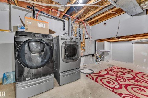 Dedicated laundry area featuring a front-load washer and dryer set, exposed ceiling joists, concrete flooring, and partial drywall finishes - 1328 80 Street, Edmonton, AB 