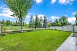 Expansive lawn area featuring a concrete patio, wood privacy fencing, and a chain-link fence bordering a paved pathway - 