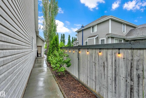 Exterior pathway featuring concrete paving, privacy fencing with string lighting, and mature landscaping - 1328 80 Street, Edmonton, AB 