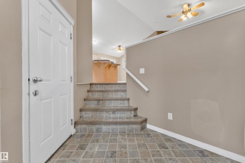 Entryway with tile flooring, a white paneled door, and a staircase featuring tile treads and a white handrail - 1328 80 Street, Edmonton, AB 