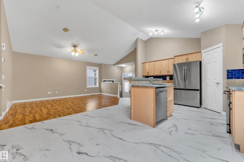Kitchen and living area featuring vaulted ceilings, wood-finish flooring, marbled tile, stainless steel appliances, and wood cabinetry with blue tile backsplash - 1328 80 Street, Edmonton, AB 