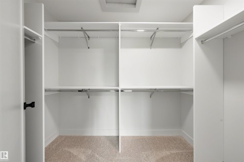 Walk-in closet with built-in shelving, chrome hanging rods, and neutral carpet flooring - 24 Grayson Green, Stony Plain, AB 
