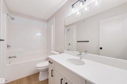 Bright bathroom featuring a white vanity with a single sink, an expansive wall-mounted mirror, and a modern light fixture - 