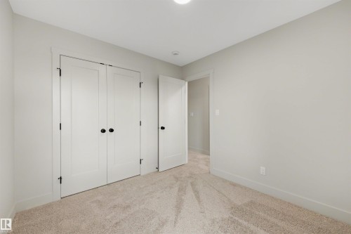 Neutral-toned room featuring a soft carpet, white baseboards, and a pair of white double doors with matte black hardware - 24 Grayson Green, Stony Plain, AB 