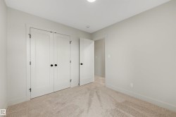 Neutral-toned room featuring a soft carpet, white baseboards, and a pair of white double doors with matte black hardware - 