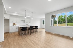 Open-concept living area featuring a kitchen island with seating, white shaker-style cabinetry, wood-finish flooring, recessed lighting, and large windows - 