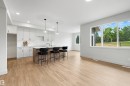 Open-concept living area featuring a kitchen island with seating, white shaker-style cabinetry, wood-finish flooring, recessed lighting, and large windows - 24 Grayson Green, Stony Plain, AB 
