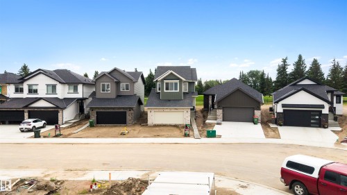 Modern residences featuring dark roofing, attached garages, and a mix of exterior siding and stone accents - 24 Grayson Green, Stony Plain, AB 