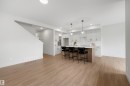 Open-concept living space featuring wood-finish flooring, a contemporary kitchen island with seating, pendant lighting, white cabinetry, and a white subway tile backsplash - 24 Grayson Green, Stony Plain, AB 
