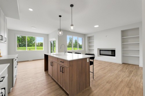 Open-concept living area featuring a kitchen island with built-in cabinetry, quartz countertops, and a stainless steel sink - 24 Grayson Green, Stony Plain, AB 