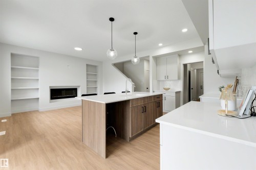 Open-concept living space featuring a central island with wood-finish cabinetry, white countertops, and pendant lighting - 24 Grayson Green, Stony Plain, AB 