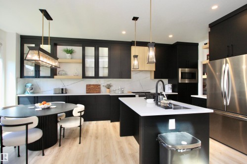 Modern kitchen featuring matte black cabinetry, light wood-finish flooring, white countertops with a matching backsplash, a stainless steel refrigerator, and a built-in microwave - 63 Penn Place, Spruce Grove, AB 