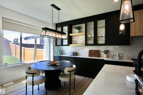 Modern kitchen featuring black cabinetry with glass-front uppers, a light-toned countertop, and a patterned backsplash - 63 Penn Place, Spruce Grove, AB 