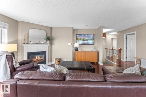 Living area featuring a white mantel fireplace, warm neutral wall tones, wood-finish flooring, a white window blind, and a wood railing with black metal spindles - 2602 Delta Road, Cold Lake, AB 