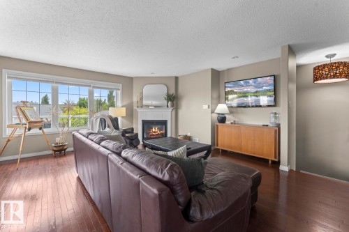 Spacious living area featuring rich wood-finish flooring, a contemporary corner fireplace with white mantel, a large window providing natural light, and neutral wall tones - 2602 Delta Road, Cold Lake, AB 