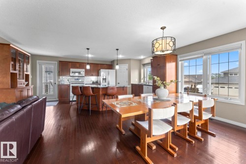 Open-concept living space featuring rich wood-finish flooring, a kitchen with dark cabinetry and stainless steel appliances, a central island with bar seating, and large windows with grid patterns - 2602 Delta Road, Cold Lake, AB 