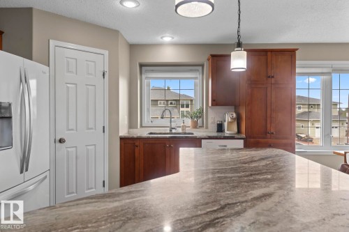 Kitchen featuring a large island with a patterned countertop, wood cabinetry, recessed lighting, a pendant light fixture, and a kitchen sink with a gooseneck faucet - 2602 Delta Road, Cold Lake, AB 