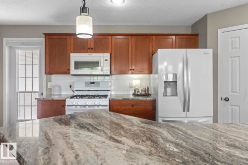 Kitchen featuring an expansive stone-finish countertop, wood cabinetry, white subway tile backsplash, and a white appliance suite - 2602 Delta Road, Cold Lake, AB 