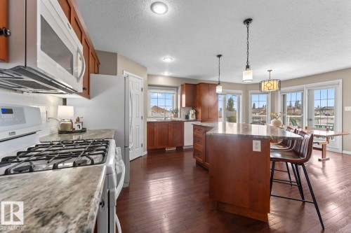 Open-concept kitchen featuring wood-finish flooring, a central island with countertop seating, recessed lighting, pendant lighting, and multiple window-paned doors - 2602 Delta Road, Cold Lake, AB 