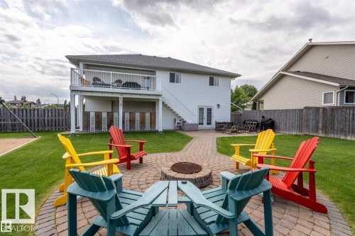 Expansive backyard featuring a circular paver patio with fire pit, surrounding lawn, and a multi-level deck with white railing - 2602 Delta Road, Cold Lake, AB 
