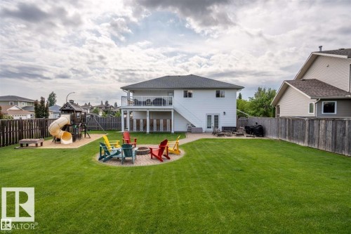 Expansive green lawn with a large paver patio, built-in fire pit, and a designated play area featuring a swing set and slide - 2602 Delta Road, Cold Lake, AB 