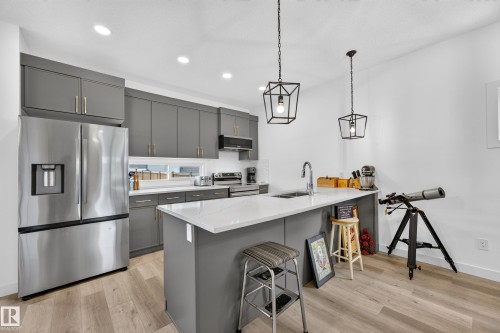 Modern kitchen featuring gray cabinetry with gold-tone hardware, stainless steel appliances, and wood-finish flooring - 104 Kidd Crescent, Leduc, AB 