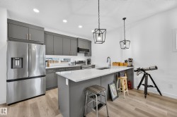 Modern kitchen featuring gray cabinetry with gold-tone hardware, stainless steel appliances, and wood-finish flooring - 