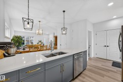 Spacious kitchen island featuring a dual basin sink, integrated dishwasher, quartz countertop, and dark gray cabinetry with gold-tone hardware - 