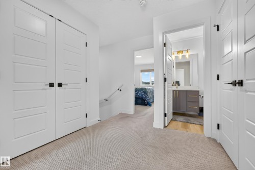Hallway featuring light-colored carpeting, white paneled doors with matte black hardware, and a white handrail - 104 Kidd Crescent, Leduc, AB 