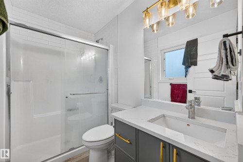 Bathroom featuring a built-in shower/tub combination with sliding glass doors, a vanity with a rectangular undermount sink, and a multi-light fixture with amber glass shades - 104 Kidd Crescent, Leduc, AB 