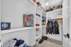 Walk-in closet featuring built-in shelving, white cabinetry, a clothing rod, and recessed lighting - 