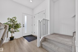 Entryway featuring a contemporary white door with frosted glass insert, wood-finish flooring, recessed lighting, and a carpeted staircase with white newel and black balusters - 