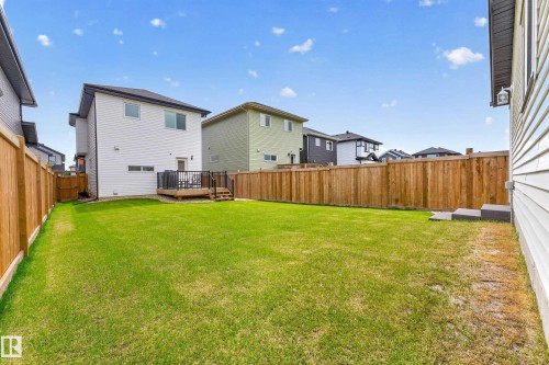 Spacious backyard featuring a large green lawn, full wood-plank fencing, and a raised wooden deck with dark railings - 104 Kidd Crescent, Leduc, AB 