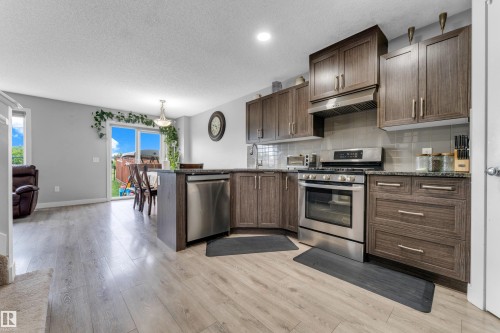 Open-concept kitchen featuring wood-finish cabinetry, stainless steel appliances, and light-toned wood-finish flooring - 1750 27 Street, Edmonton, AB 