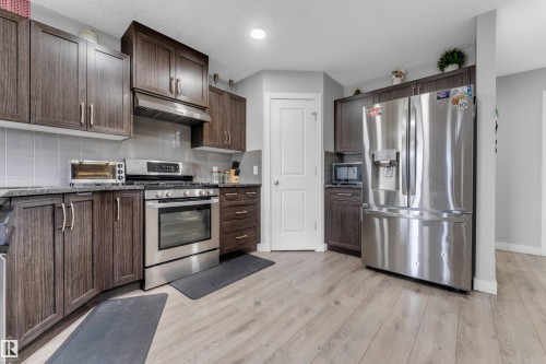 Kitchen featuring wood-finish cabinetry, stainless steel appliances, granite-look countertops, a tile backsplash, and light wood-finish flooring - 1750 27 Street, Edmonton, AB 