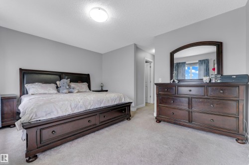 Carpeted bedroom with light gray walls, an overhead flush-mount light fixture, and a window with blue curtains - 1750 27 Street, Edmonton, AB 